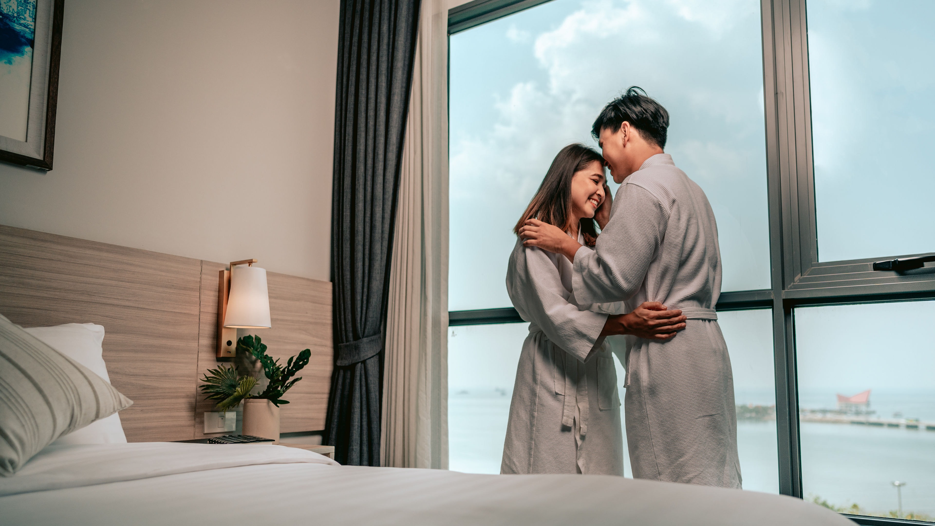 Asian couple is kissing their cheeks in window in their bedroom.