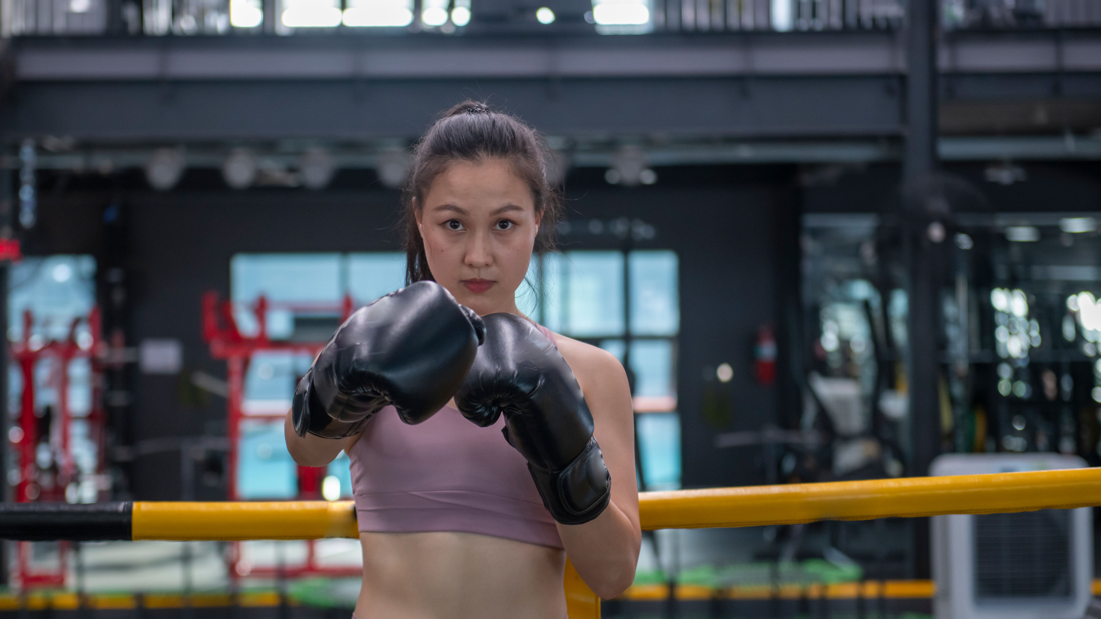 A woman stands in a boxing ring with black gloves on