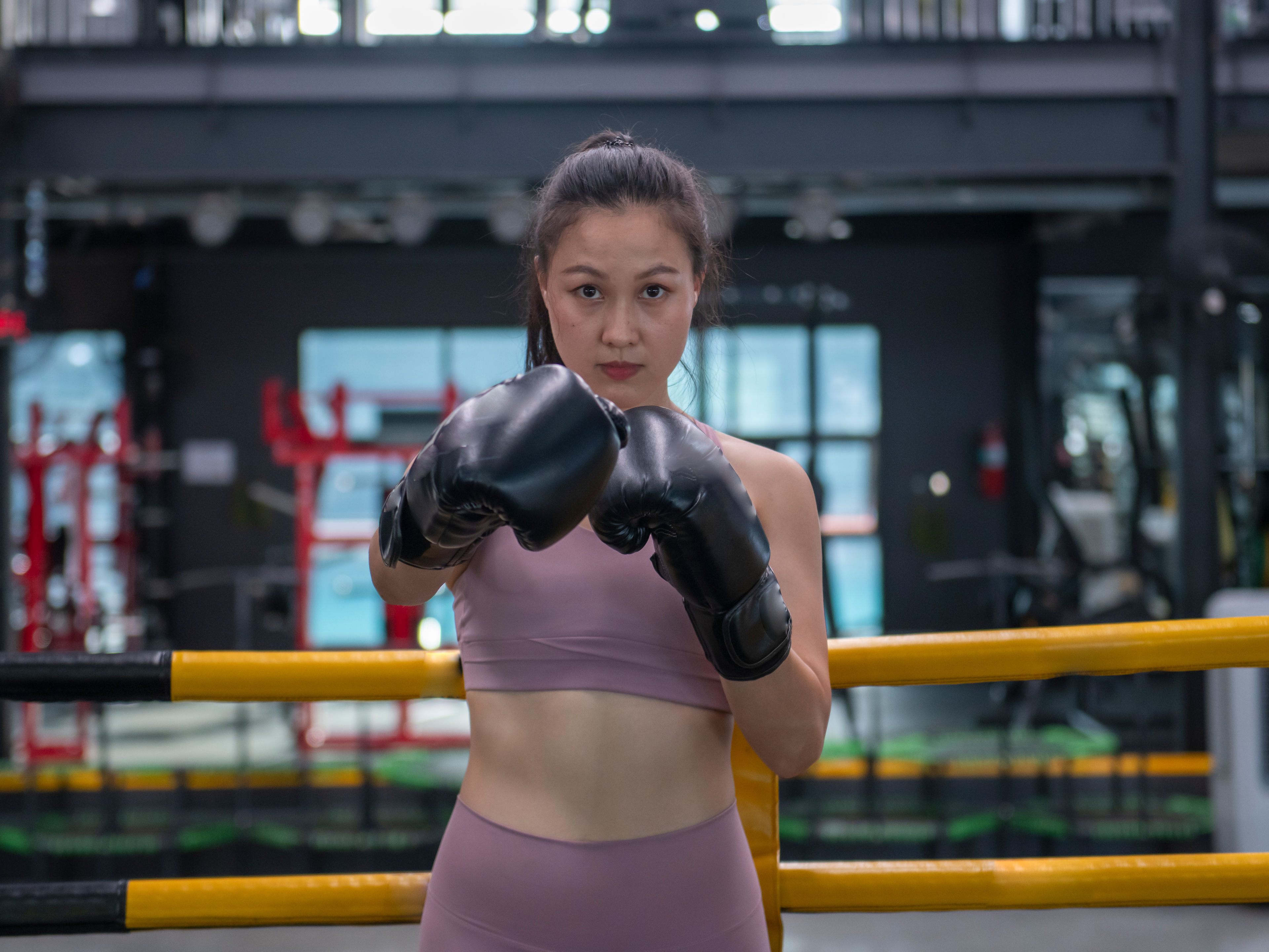 A woman stands in a boxing ring with black gloves on