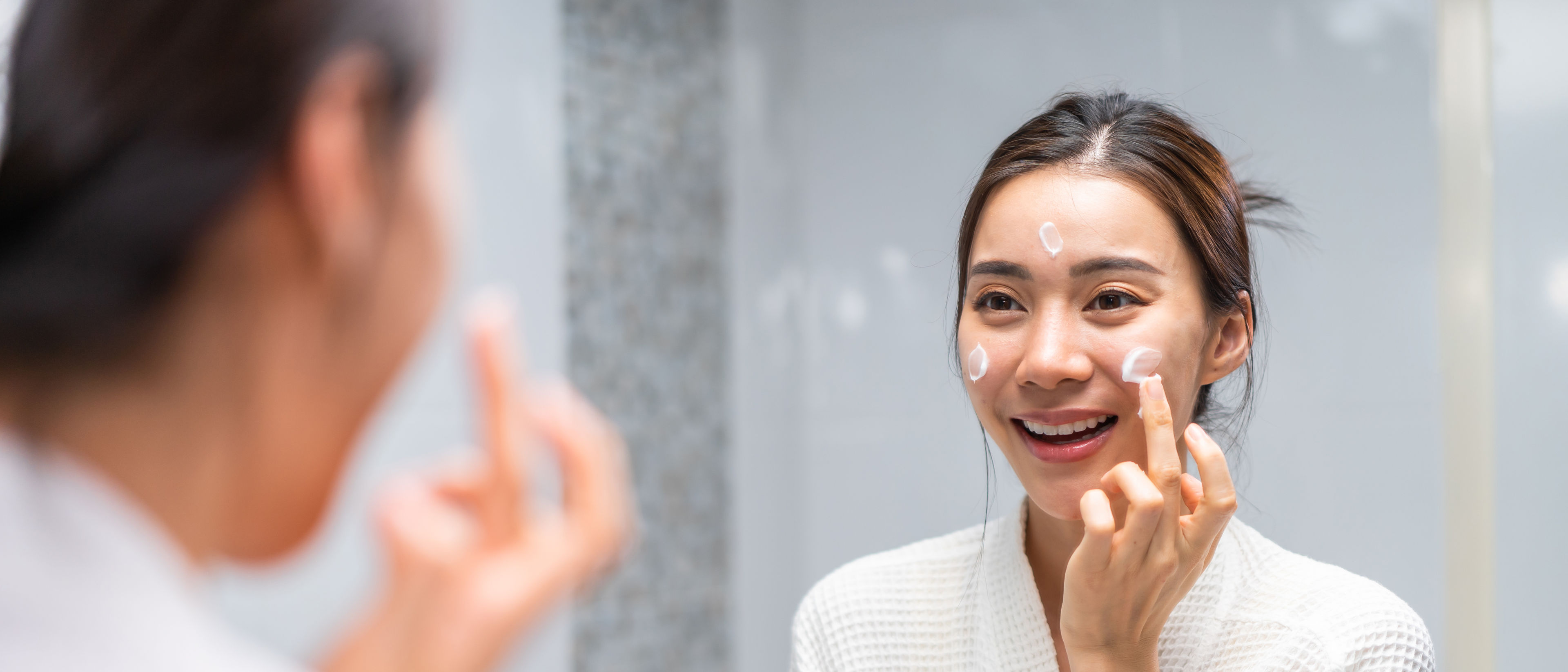 Woman applies cream to her face.