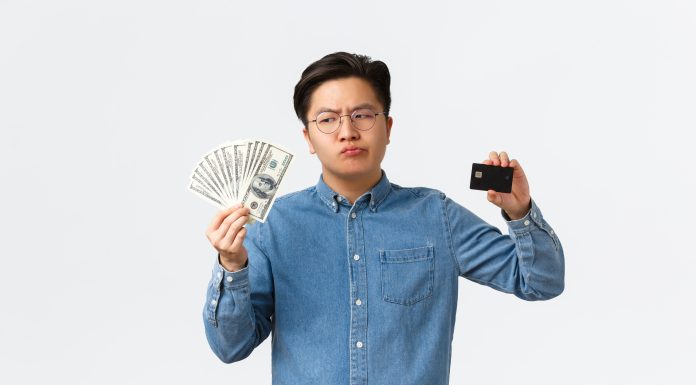 Asian guy with glasses holding a fan of cash on one hand and a card on the other.